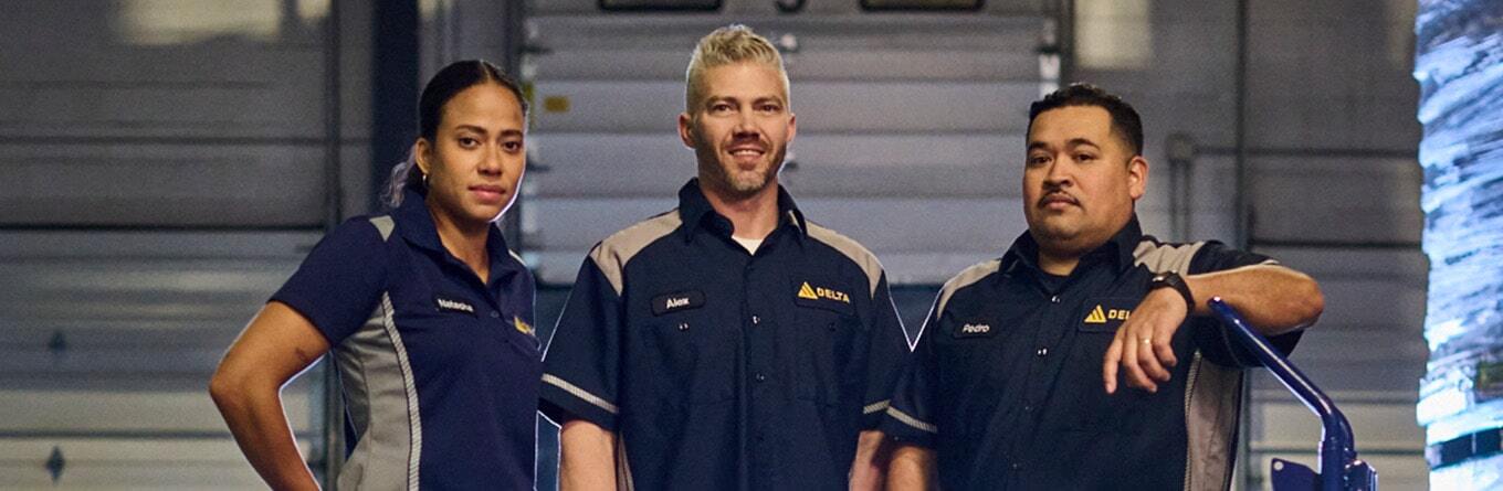 Three employees of a packaging and logistics company wear navy blue and grey Spotlite MV work shirts and polo shirts as part of a custom uniform program provided by UniFirst.