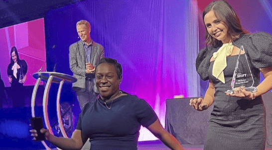 Stephanie Roman and Kolyn Johnston step off the stage after receiving an award from Seismic on behalf of UniFirst for being a Sales Enablement Leader.