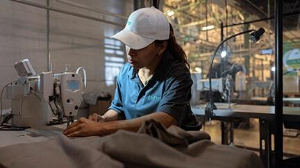 A UniFirst production Team Partner wearing a Micro Piqué Polo Shirt and baseball with the UniFirst logo repairs garments as part of the gurantee that comes with a UniFirst uniform rental program.