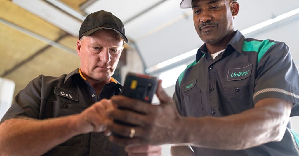 UniFirst representative showing a uniform rental service customer information on a handheld device