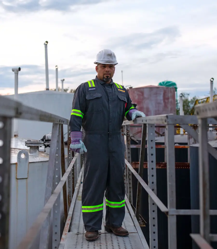 Energy and utilities industry worker stops and stands on equipment wearing UniFirst flame resistant and enhanced visibility coveralls