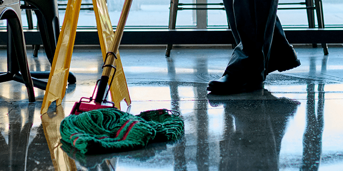 Low-shot image of person's wearing dark pants and work shoes, mopping floor with UniFirst Wet Mop.