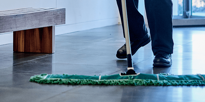 Low-shot image of person's wearing dark pants and work shoes, mopping floor with UniFirst Dry Mop