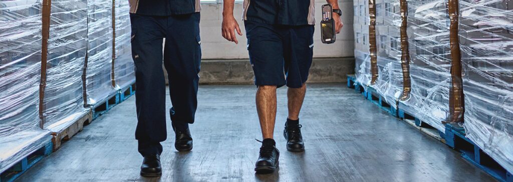 Industrial wholesale workers walking in a warehouse wearing UniFirst enhanced visibility pants.