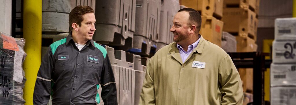 A UniFirst RSR walking and discussing work uniform rental service with his customer in a warehouse setting