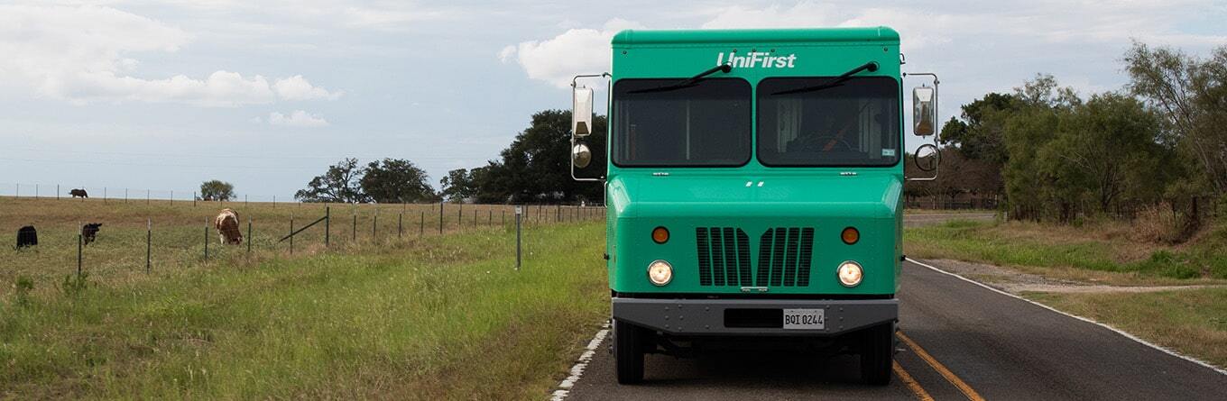 A UniFirst Route Truck is driving down an open country road to deliver hygienically cleaned uniforms to customers.