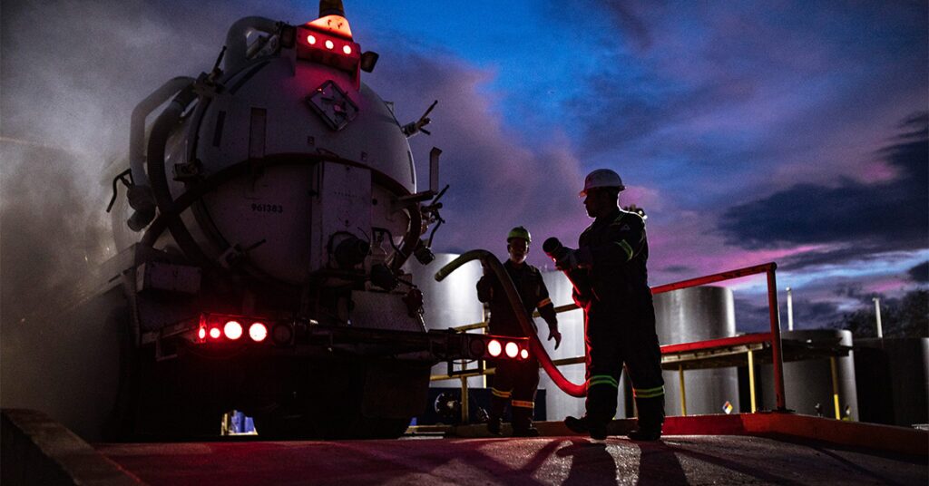 Workers in the energy and utilities industry performing job tasks near oil truck while wearing UniFirst industrial workwear.