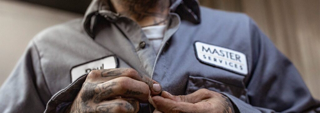 A close up images of a man buttoning up a uniform work shirt